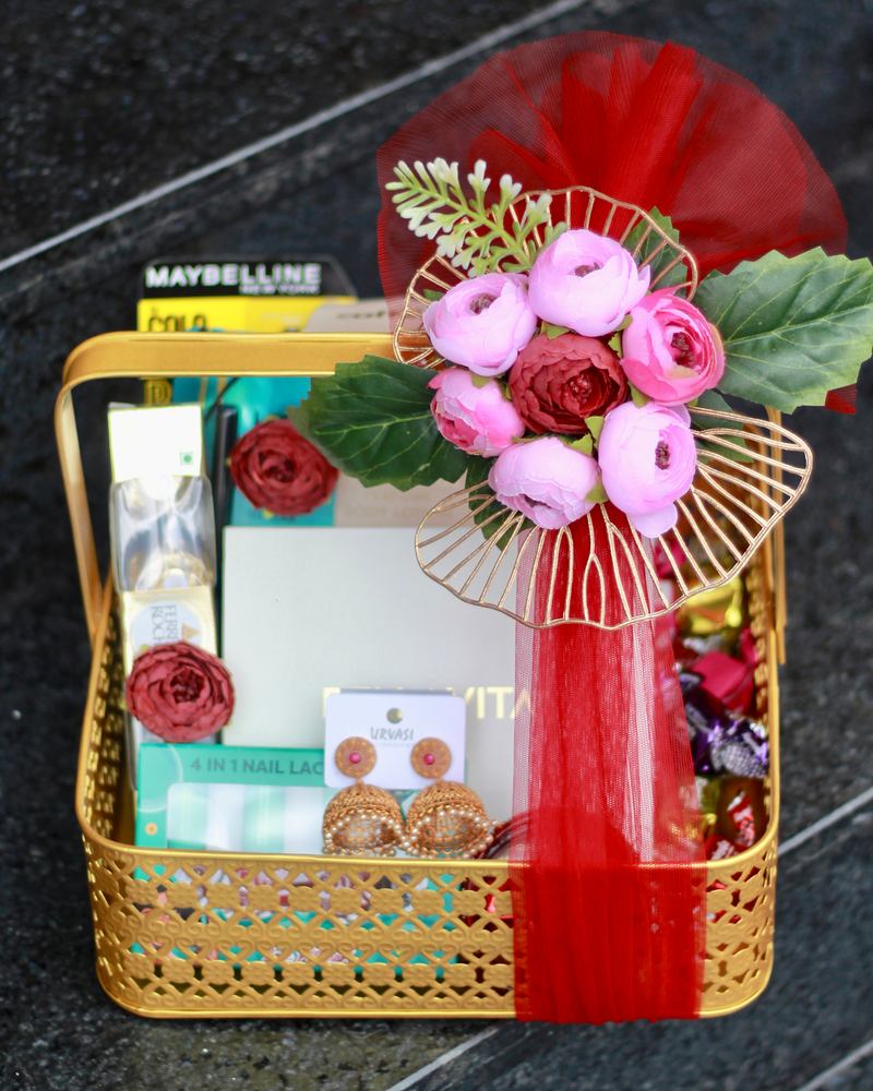 Customised gift hamper in a gold basket with red tulle, pink ranunculus, earrings and cosmetics