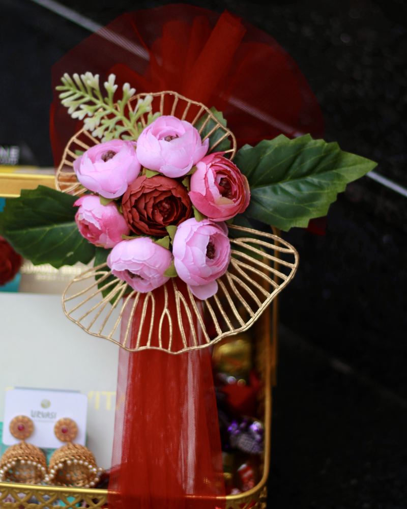 Close-up of pink ranunculus and a gold wire fan on a gift hamper wrapped in red tulle