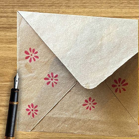 Kraft envelope hand-stamped with red flowers, beside a fountain pen